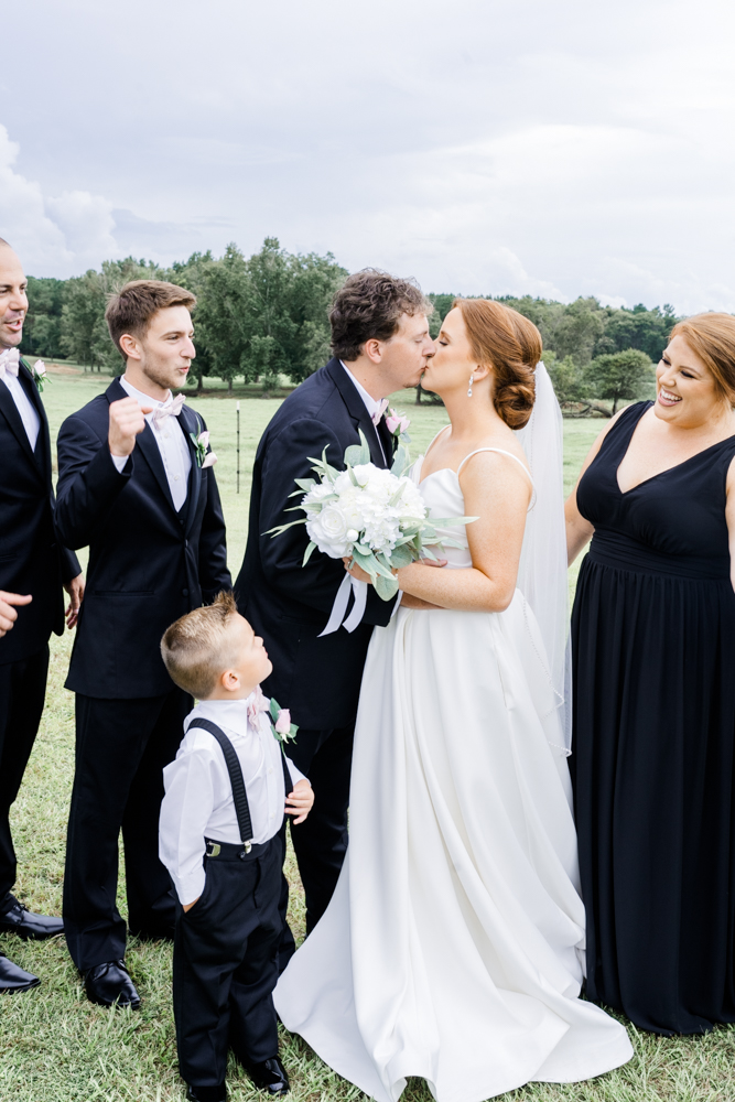 bride and groom kissing while their bridal party cheers around them outside