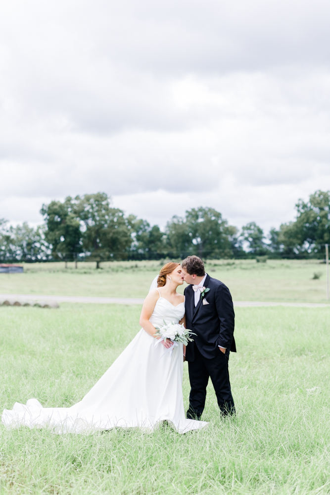 bride and groom holding hands kissing in a green field 