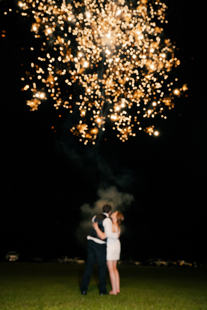 bride and groom kiss under fireworks during their sendoff