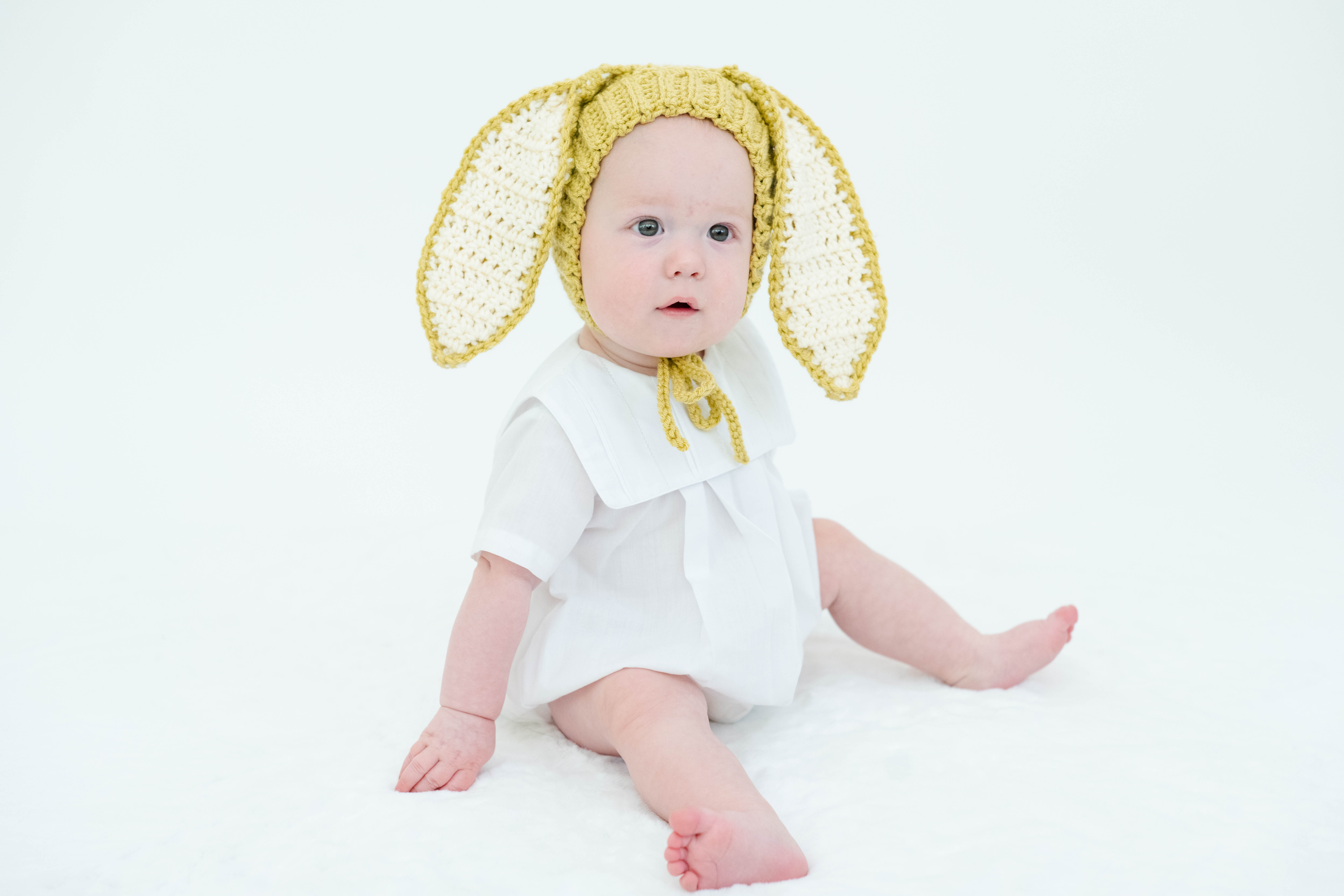 infant boy poses in front of camera in white heirloom bubble with yellow bunny bonnet 