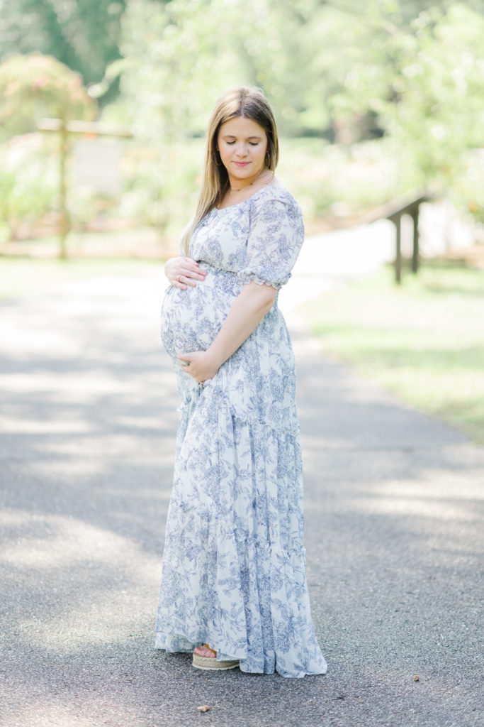 an expectant mama in a blue and white floral dress holds her belly while looking down her left shoulder