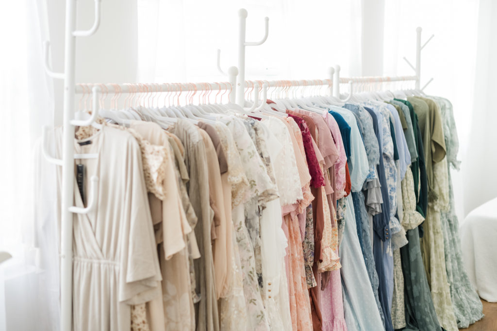 an assortment of dresses in a variety of colors hanging on white clothing racks in a white studio